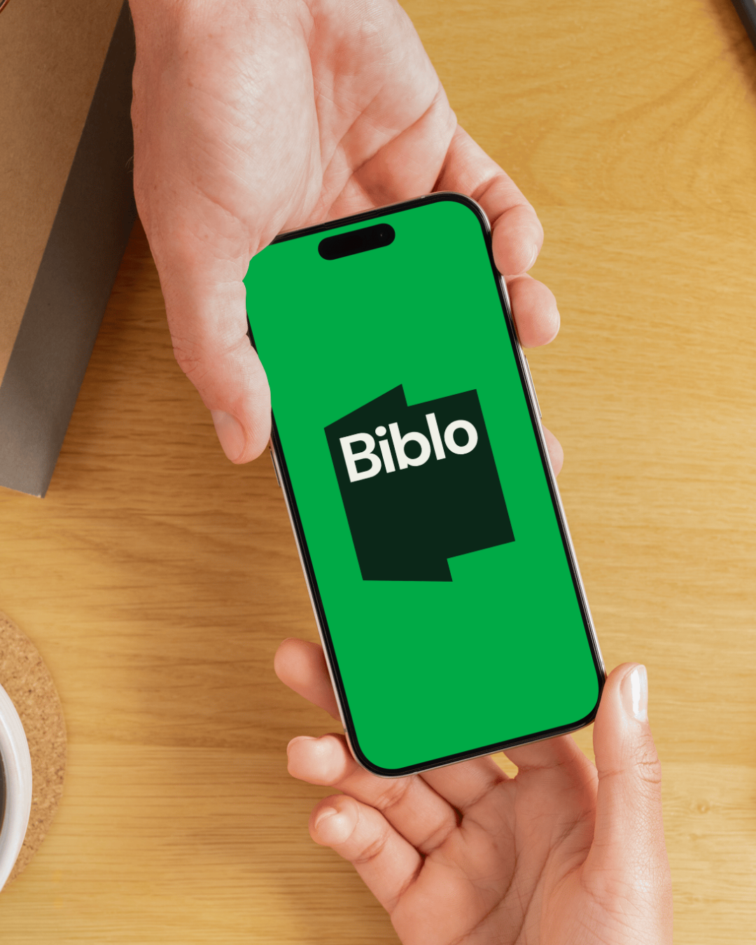 En person holder en smartphone med Biblo app-skjerm som har en grønn bakgrunn og to overlapping svarte bokser med hvit tekst.