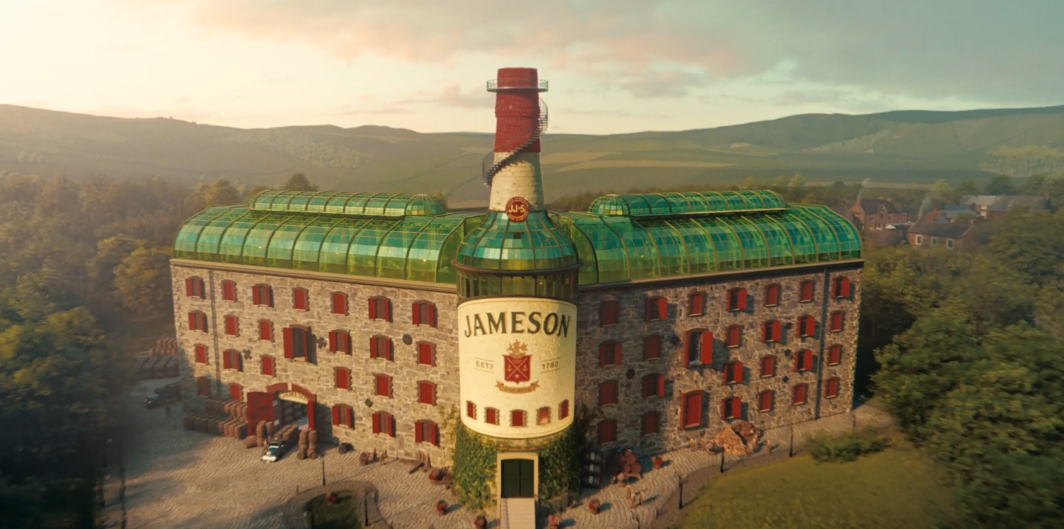 Large building resembling a whiskey distillery with a green roof, a painted whiskey bottle with 'Jameson' logo on it, and a chimney shaped like a whiskey bottle.