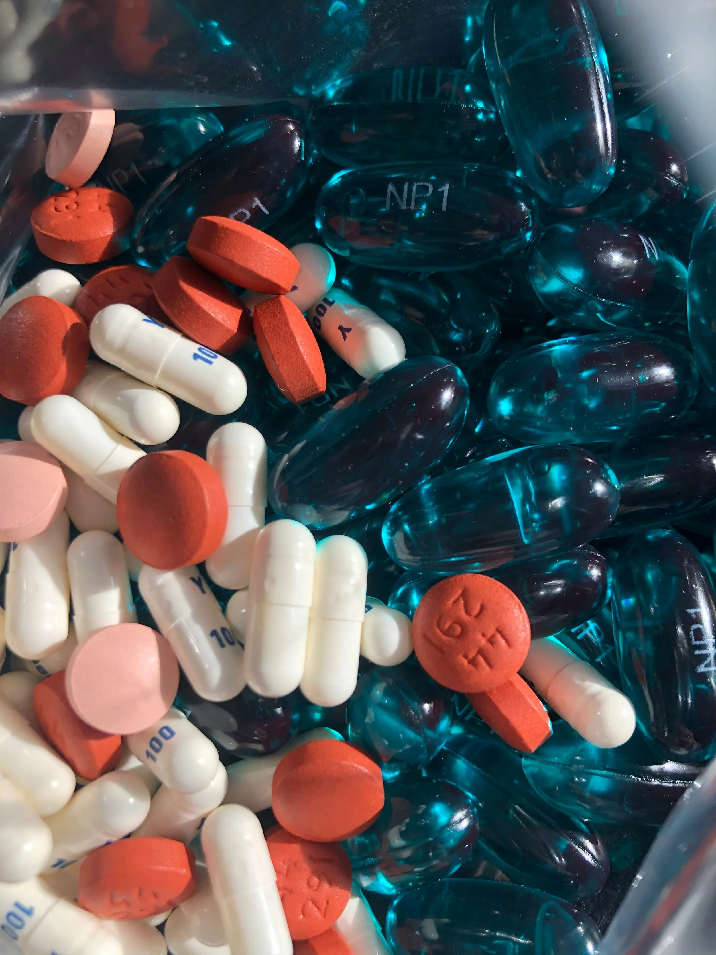 A collection of various pills and capsules, including white capsules with '10' printed on them, round orange tablets, and blue gel capsules.
