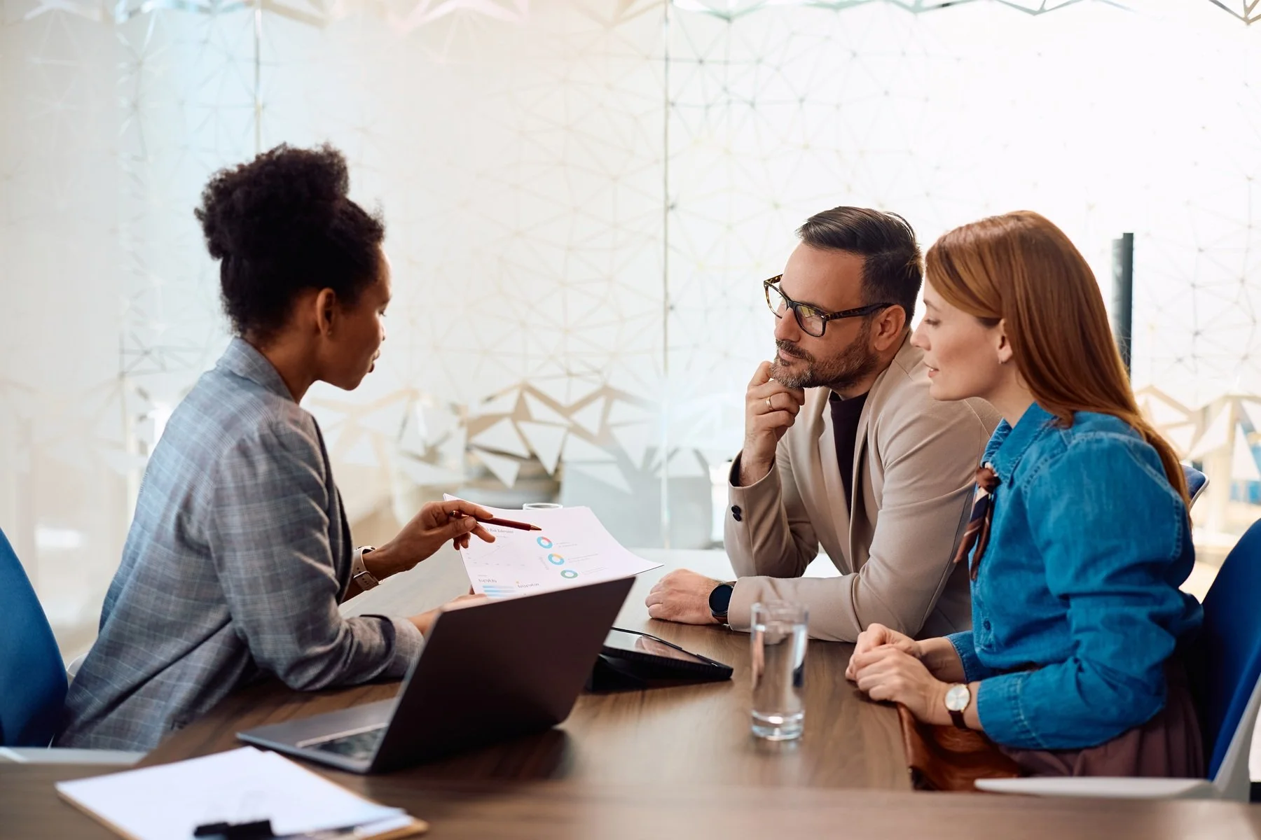 A technical consultant reviews data sheets and analytical insights with an engaged team of stakeholders around a modern conference table.