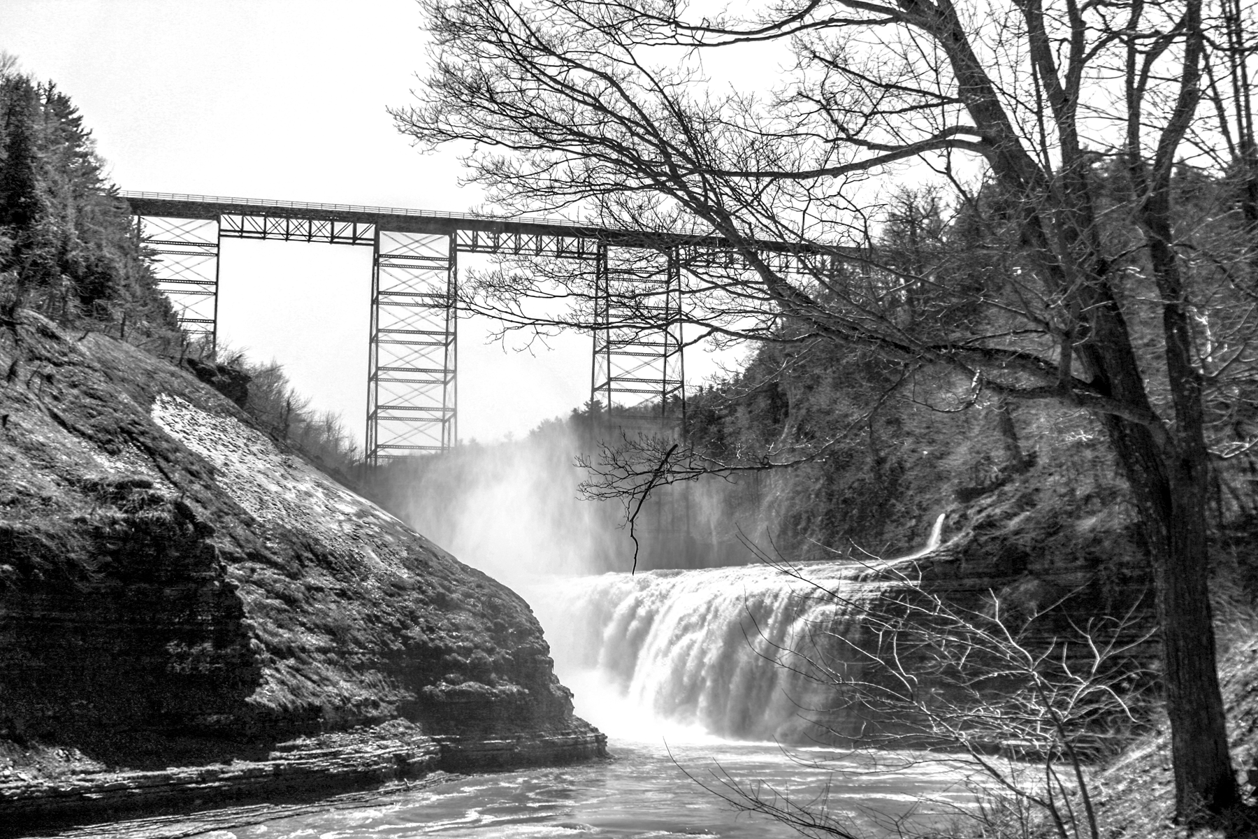 Steel railway bridge spanning a gorge with waterfall below, black and white photograph.
