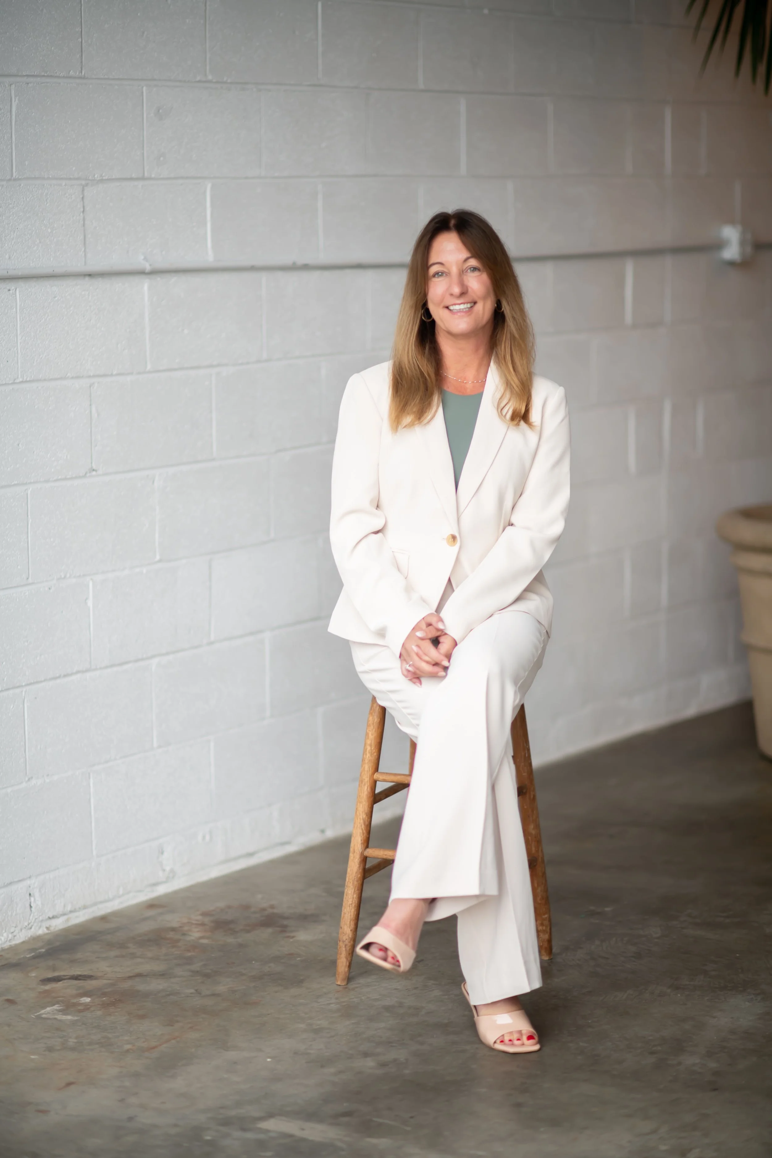 Founder of Bloom Consulting, Heather, sitting on stool while wearing a white suit and smiling
