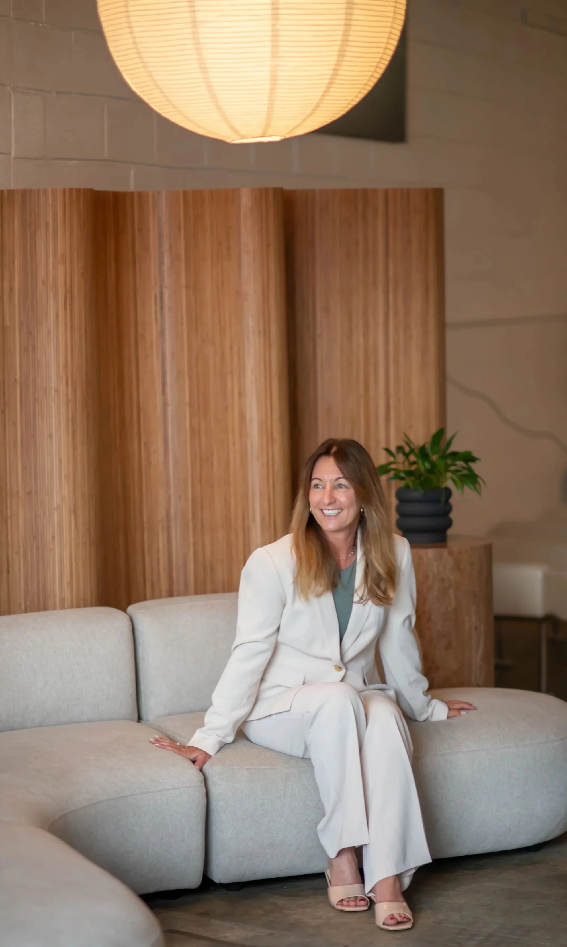 Founder of Bloom, Heather, in white suit sitting on couch smiling
