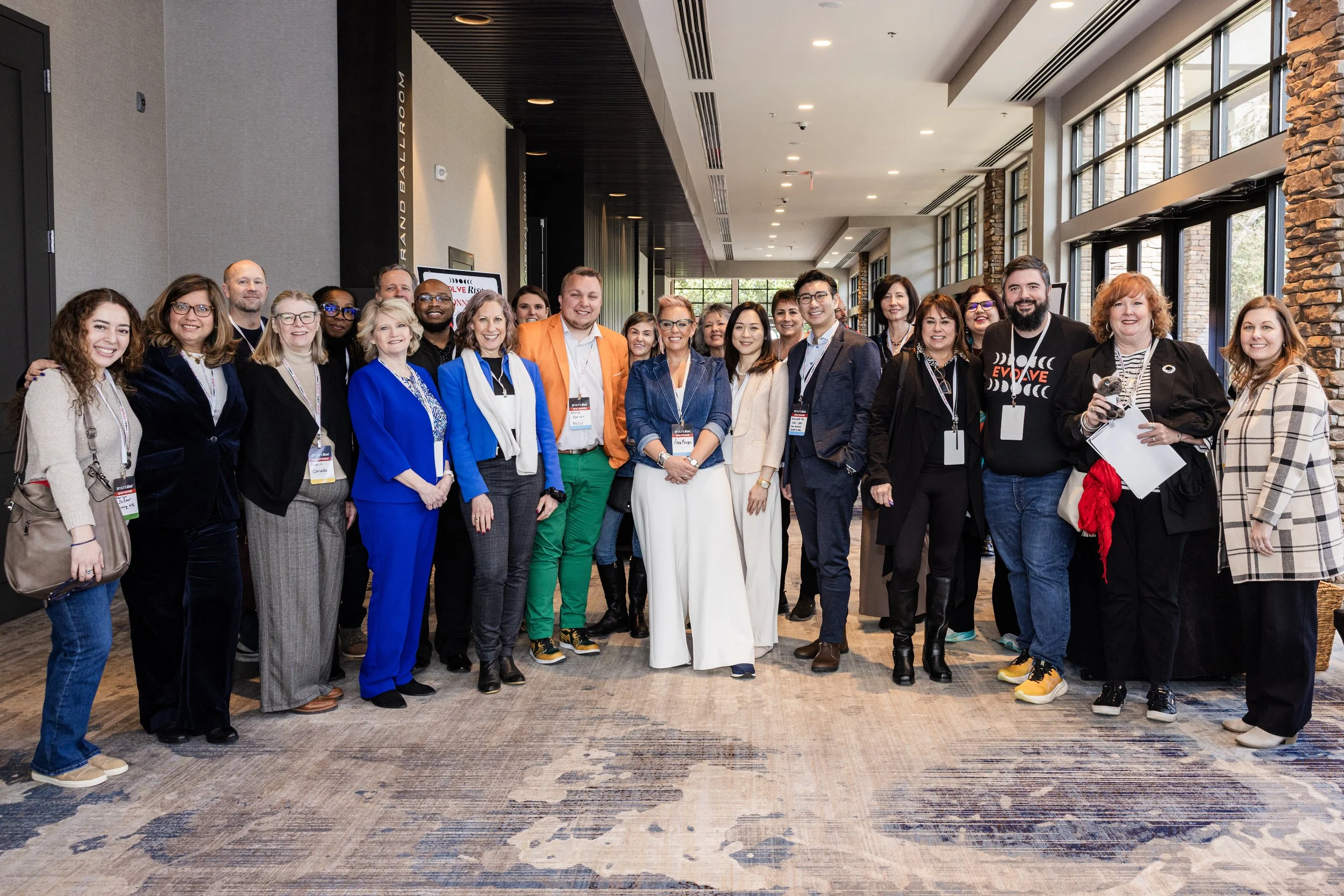 Group of diverse professionals posing together in a modern indoor setting with large windows and exposed brick walls, attending a conference or workshop.