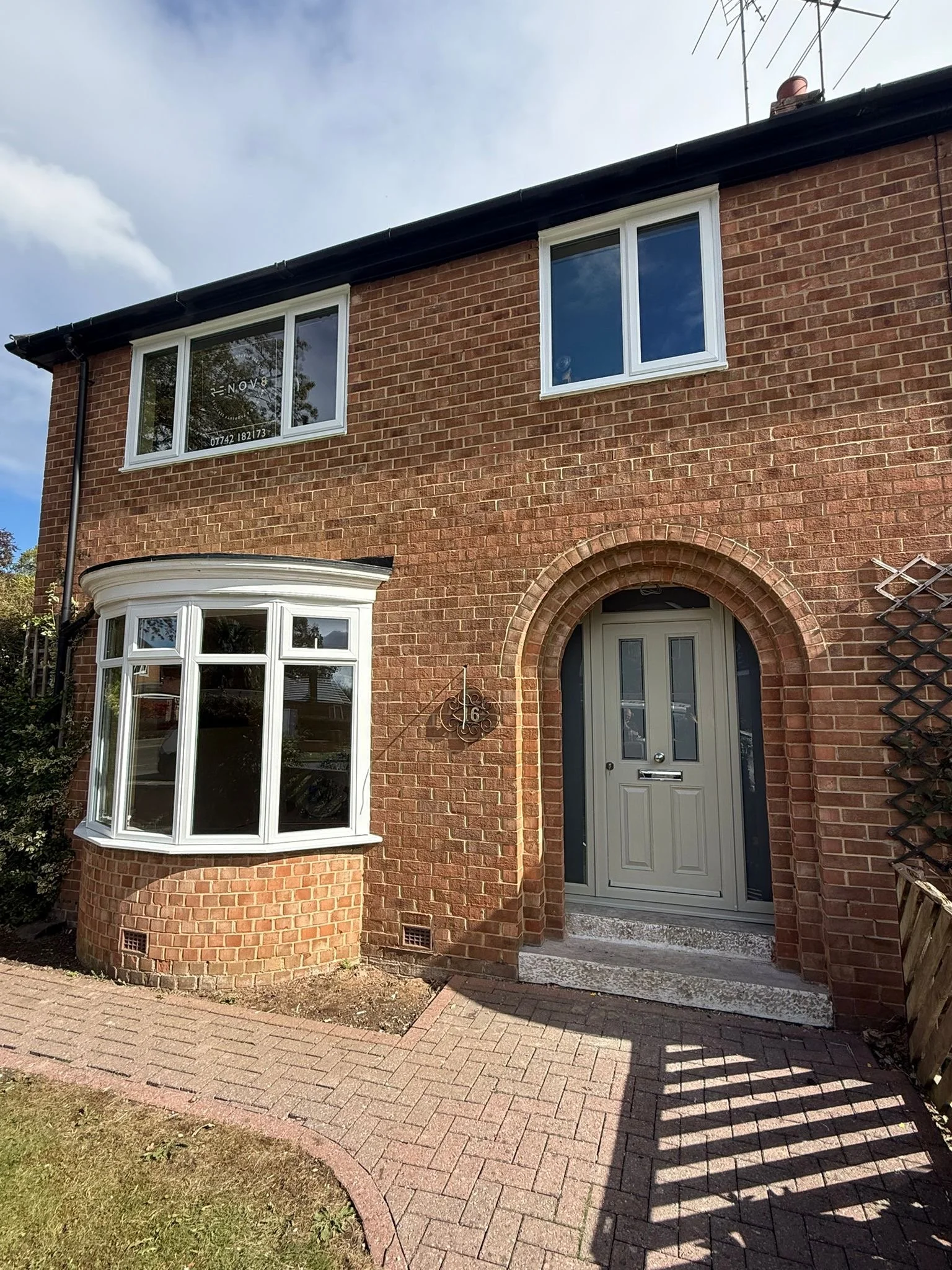 The front of a brick house with a bay window, a double-door entryway, and a small garden area with a pathway and grass.