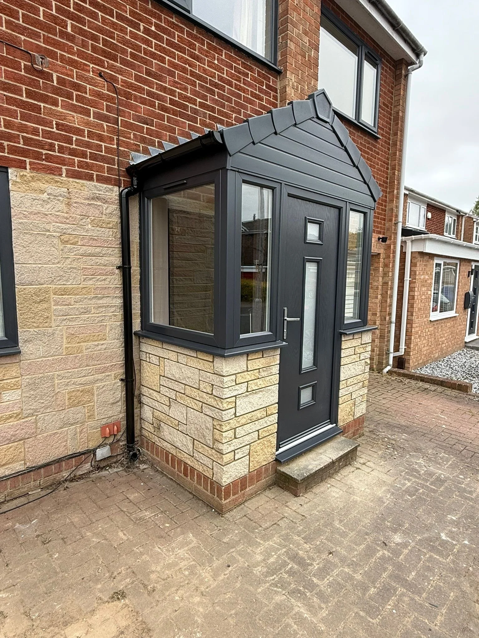 Exterior of a brick house with a black glass porch and a small set of steps, outside paving, and a paved driveway.