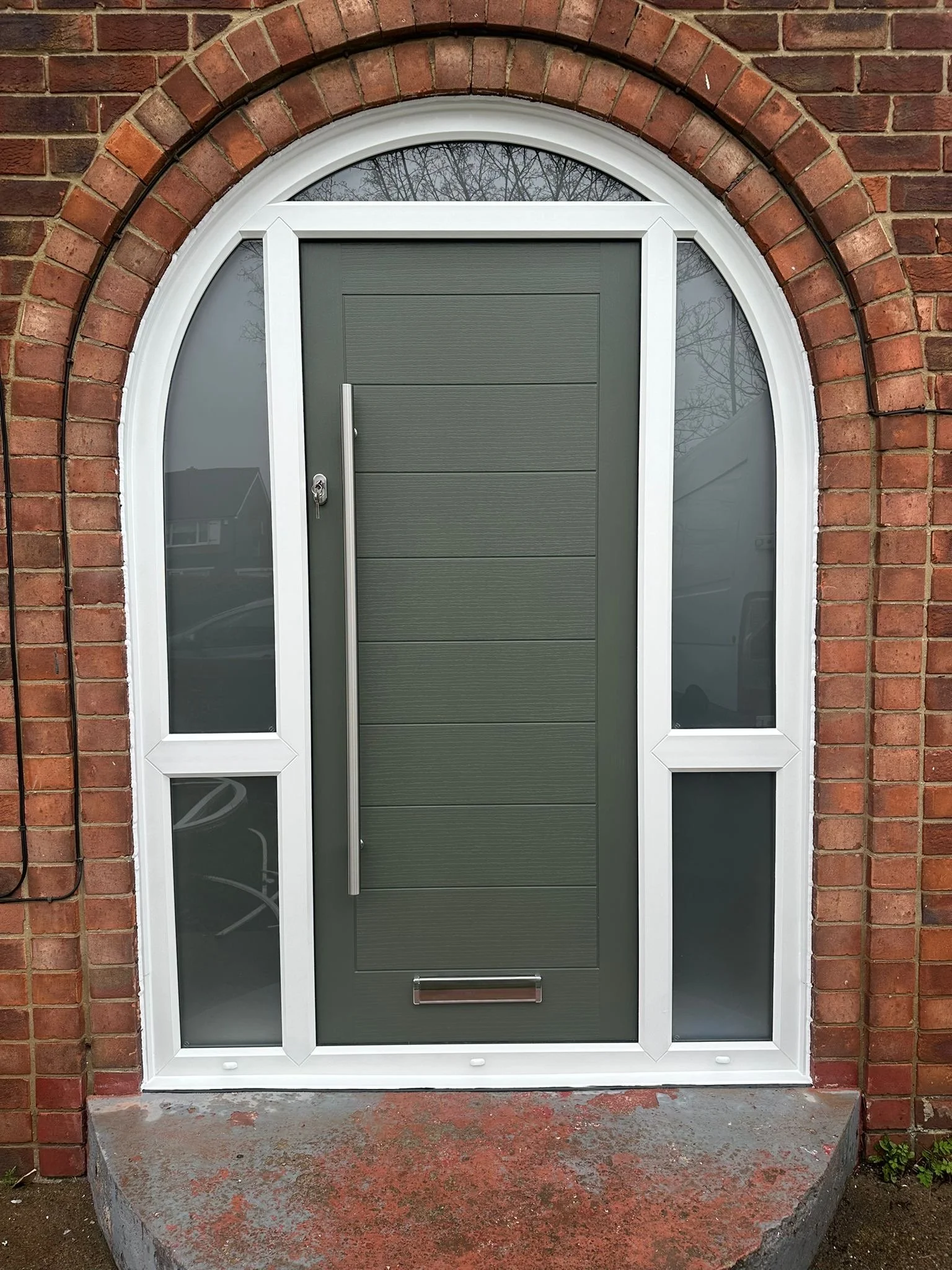 Front door of a house with a brick archway and a gray door with sidelights.