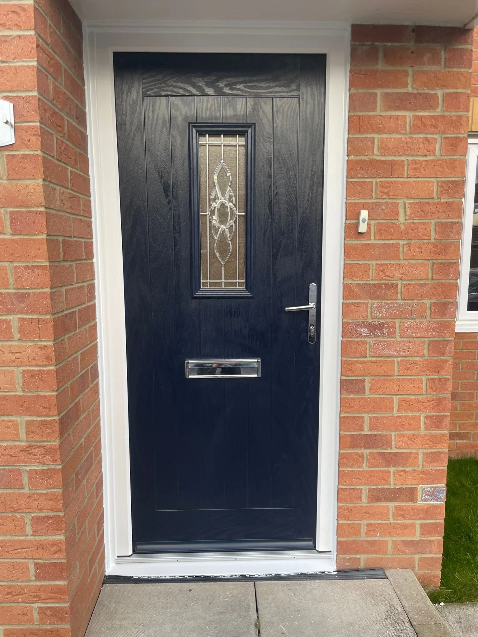 Black front door with decorative glass insert, surrounded by white trim, with brick walls on either side and a concrete step in front.