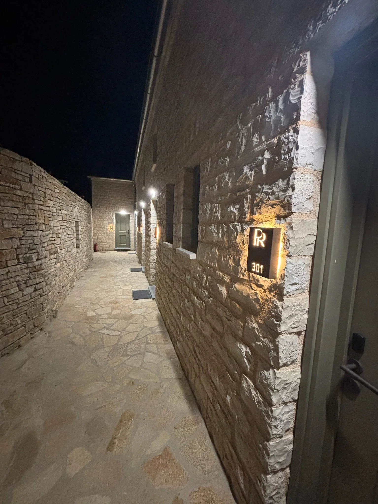 Night view of a stone alleyway with LED lights on the exterior wall leading to a door at the end.