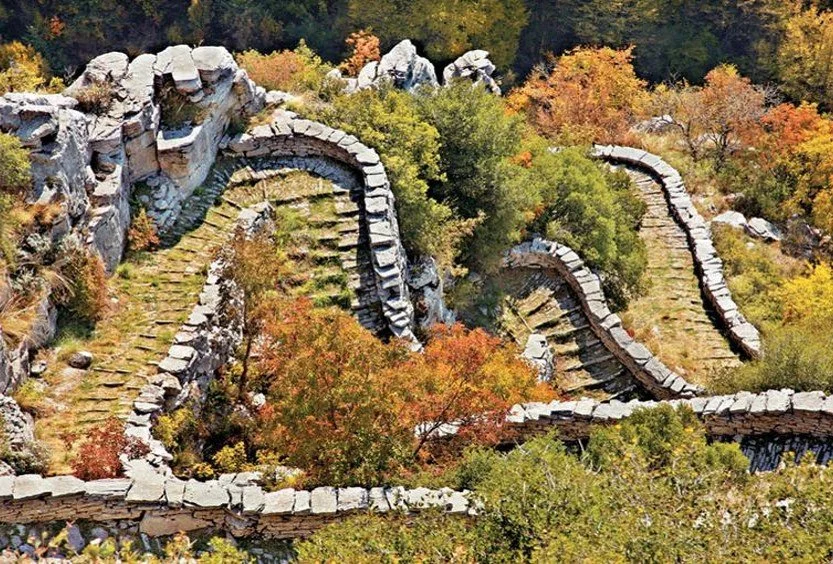 Abandoned stone staircase winding through autumn foliage in a forested area.