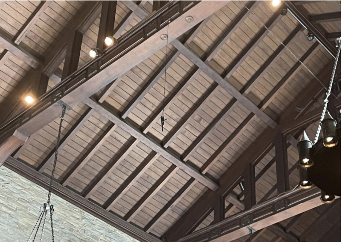 Interior view of a wooden ceiling with exposed beams, a hanging microphone, and metal chandeliers.