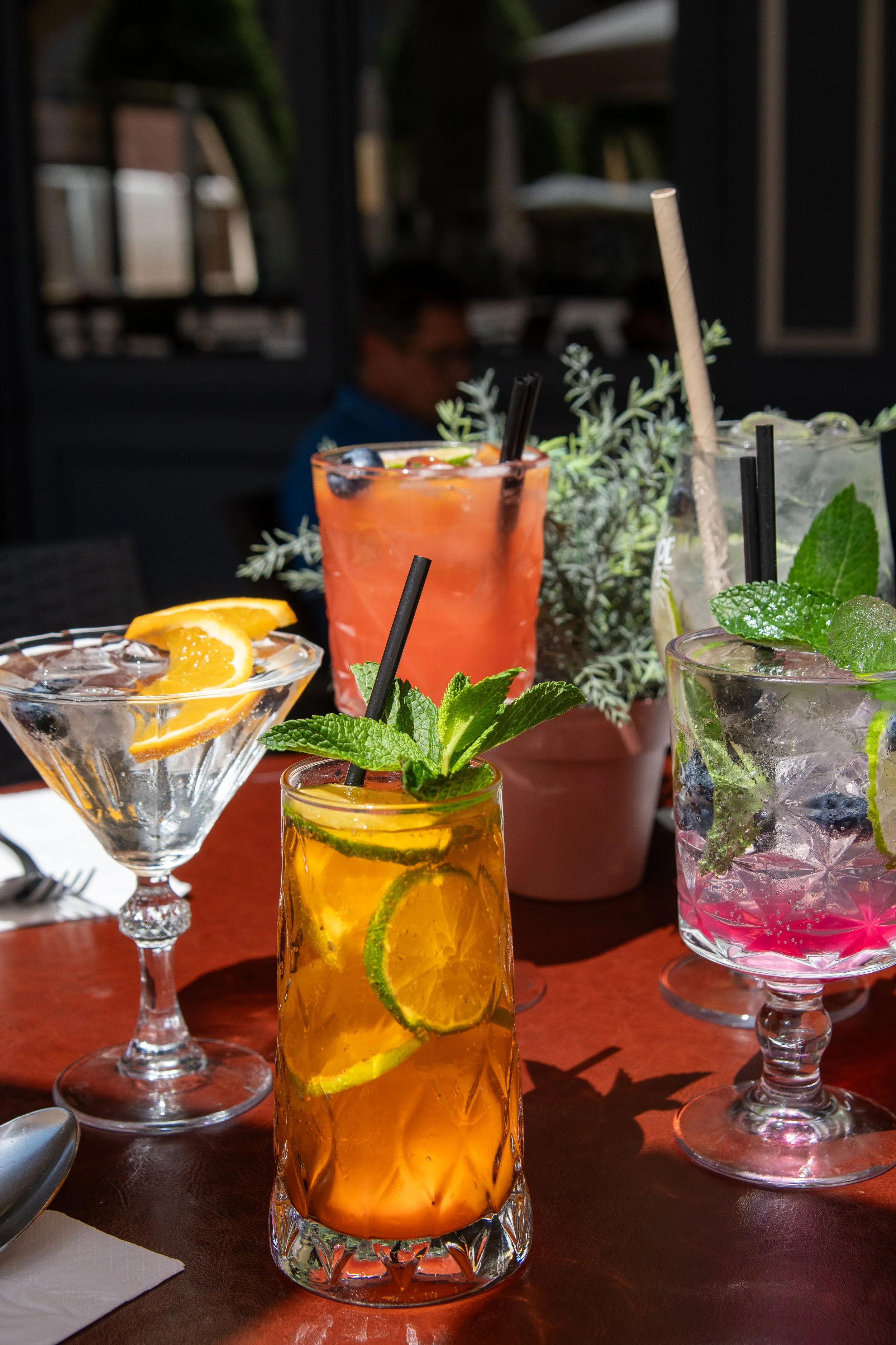 Une sélection de différents cocktails colorés avec des fruits et des herbes sur une table en bois, ambiance extérieure