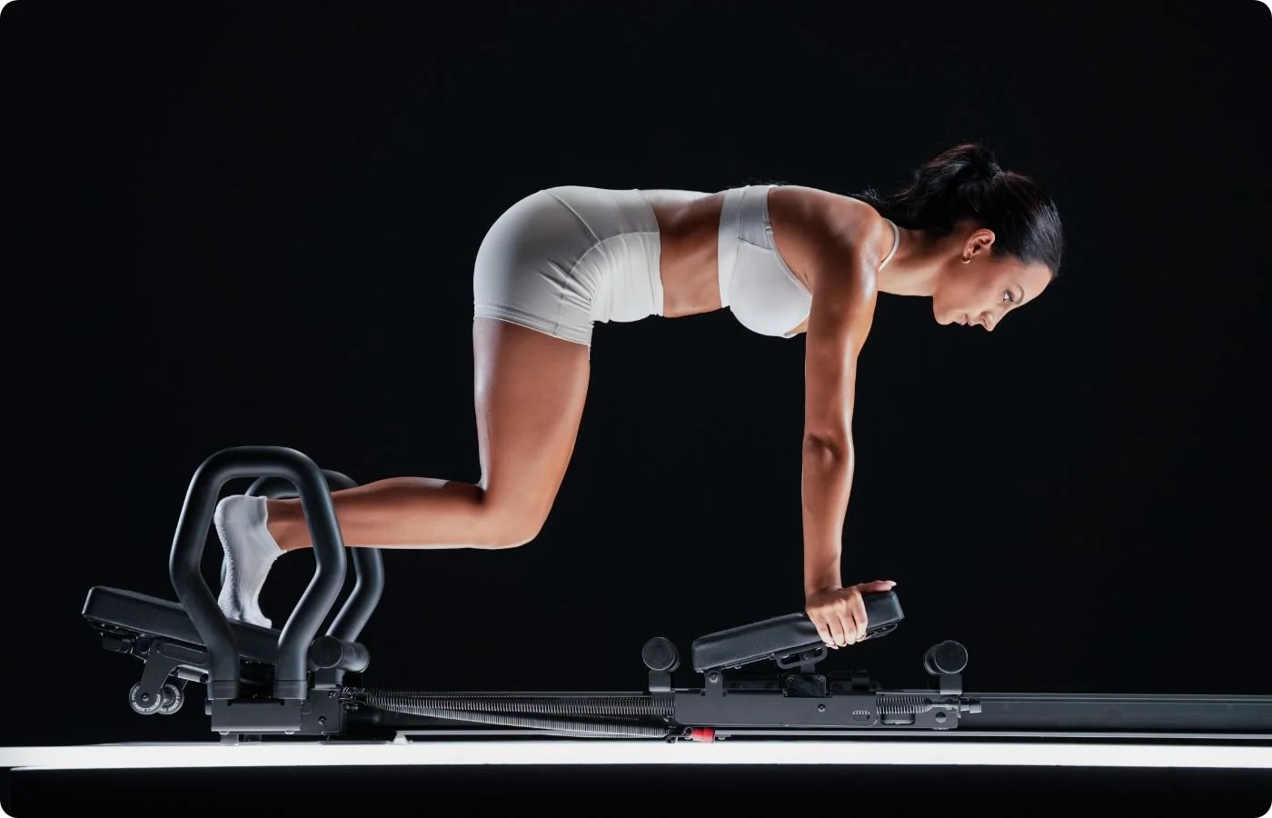 A woman in athletic wear performing a plank exercise on a specialized exercise machine with a black background.