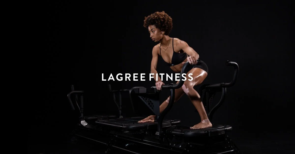 A woman with curly hair in a black sports bra and shorts using a stair climber exercise machine against a black background, with the text 'LAGREE FITNESS' overlaid.