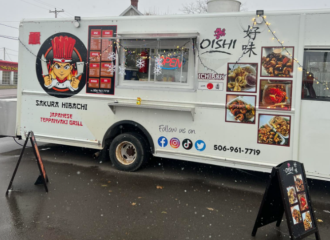 Food truck decorated with Christmas lights and snow, featuring Japanese dishes and restaurant branding, with menu and social media icons.