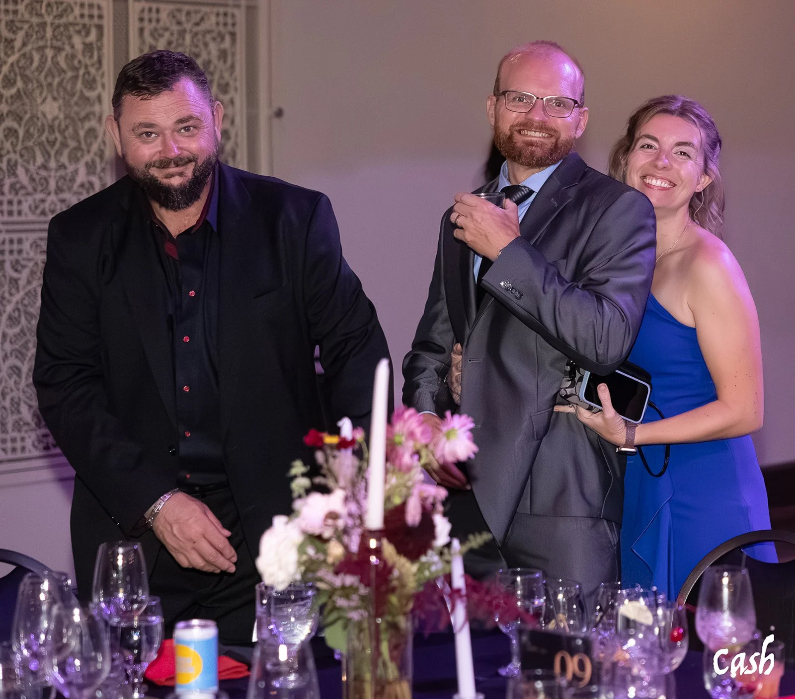 Four people smiling at a formal event, standing near a table with wine glasses and a floral centerpiece.