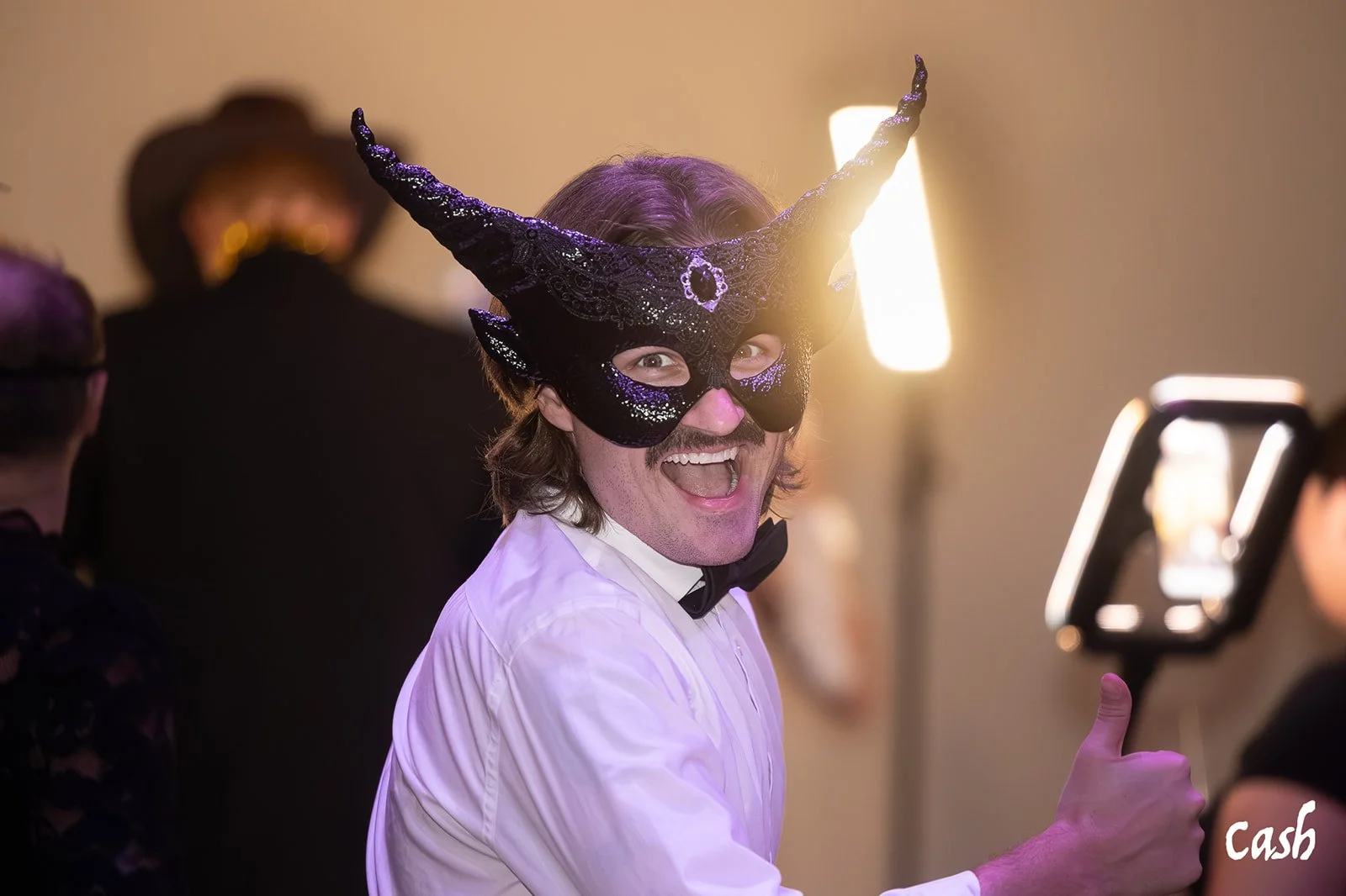 Man wearing a black and purple horned mask and a white dress shirt, smiling and giving a thumbs-up