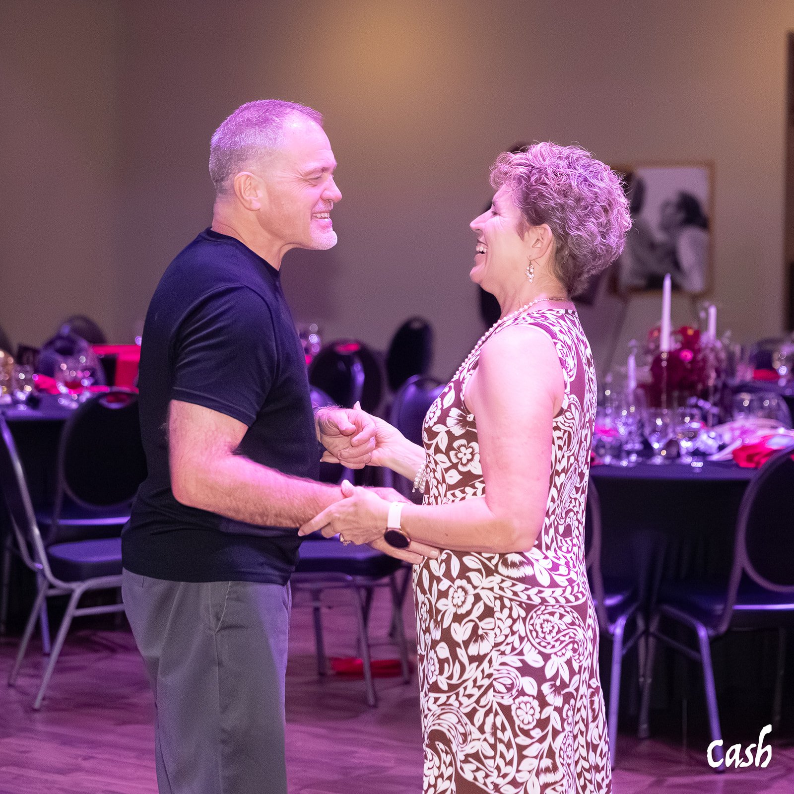 A man and an older woman are dancing and smiling at each other in a decorated event hall.
