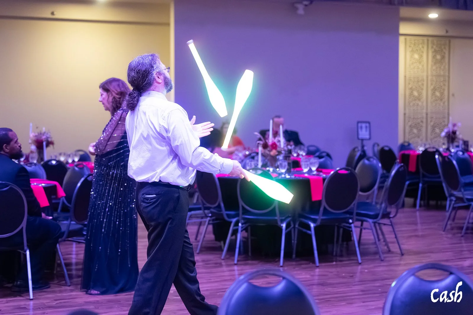 A man juggles LED clubs at a formal event inside a decorated banquet hall.