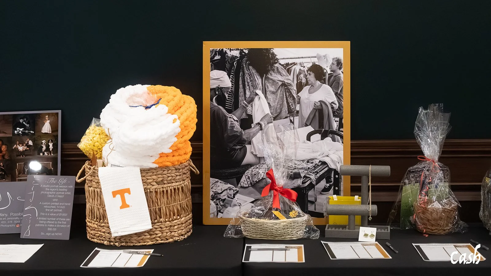 A table showcasing various gift items, including crocheted yarn art, wrapped baskets, jewelry, and photographs, set against a dark background.