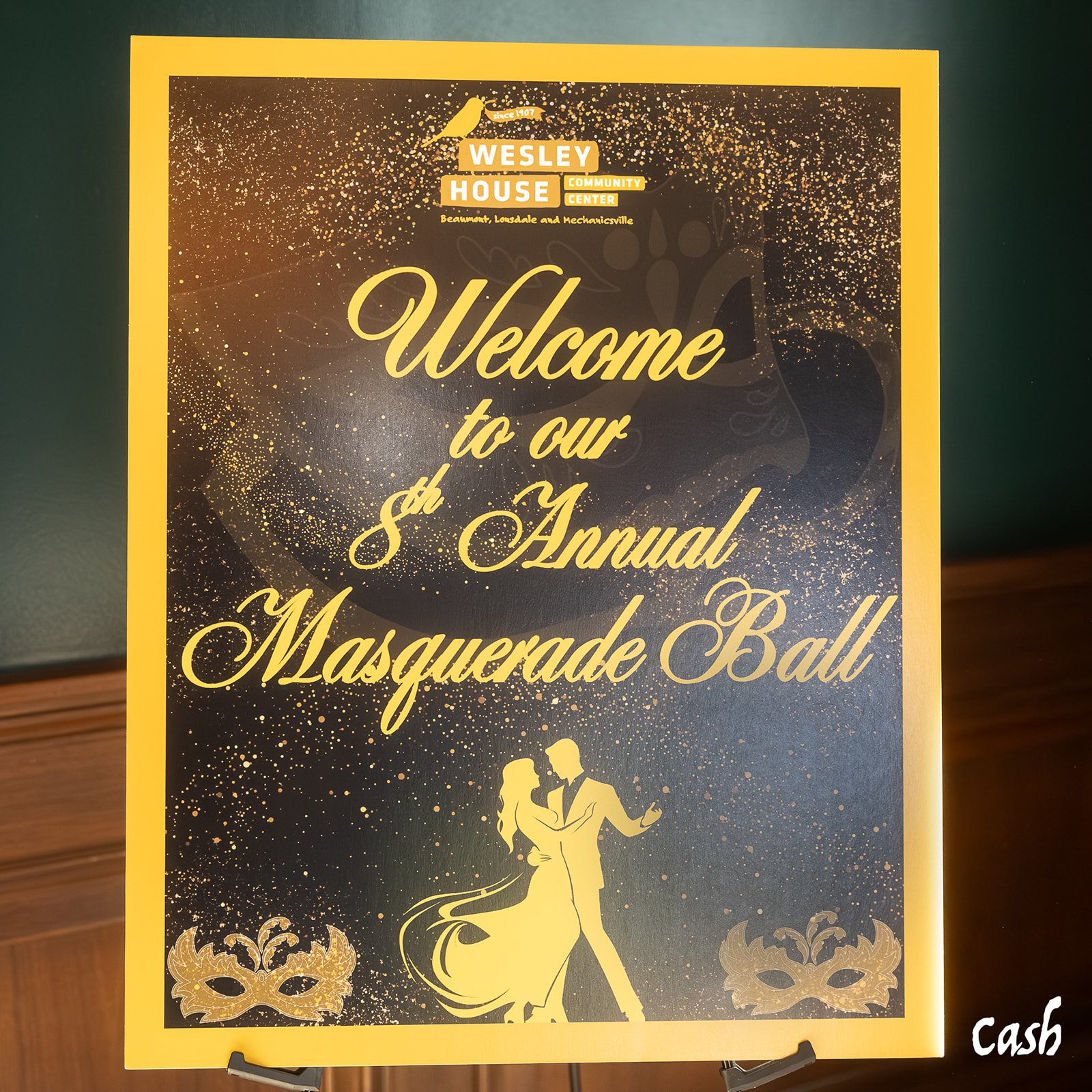 A poster for the Wesley House Community Center's 8th Annual Masquerade Ball, featuring a dancing couple silhouette, gold decorative elements, and a black background with gold confetti-like patterns.