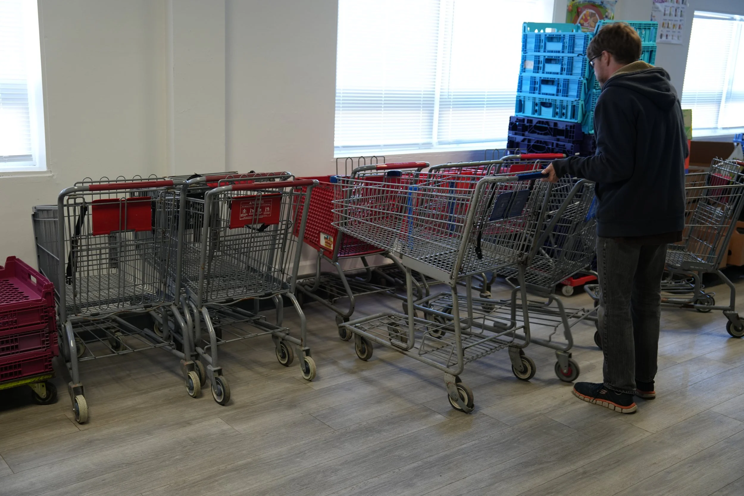 A person shopping for carts in a store, surrounded by empty shopping carts and crates, with large windows and shelves in the background.