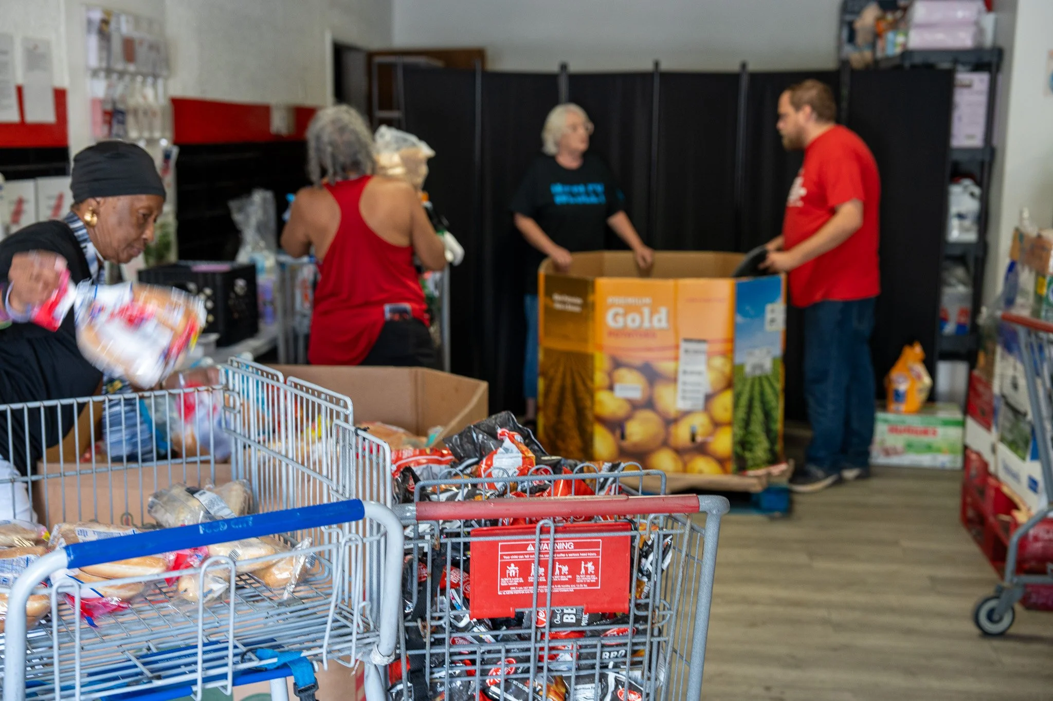 People volunteering at a food bank, organizing and packing food items into large boxes and carts.