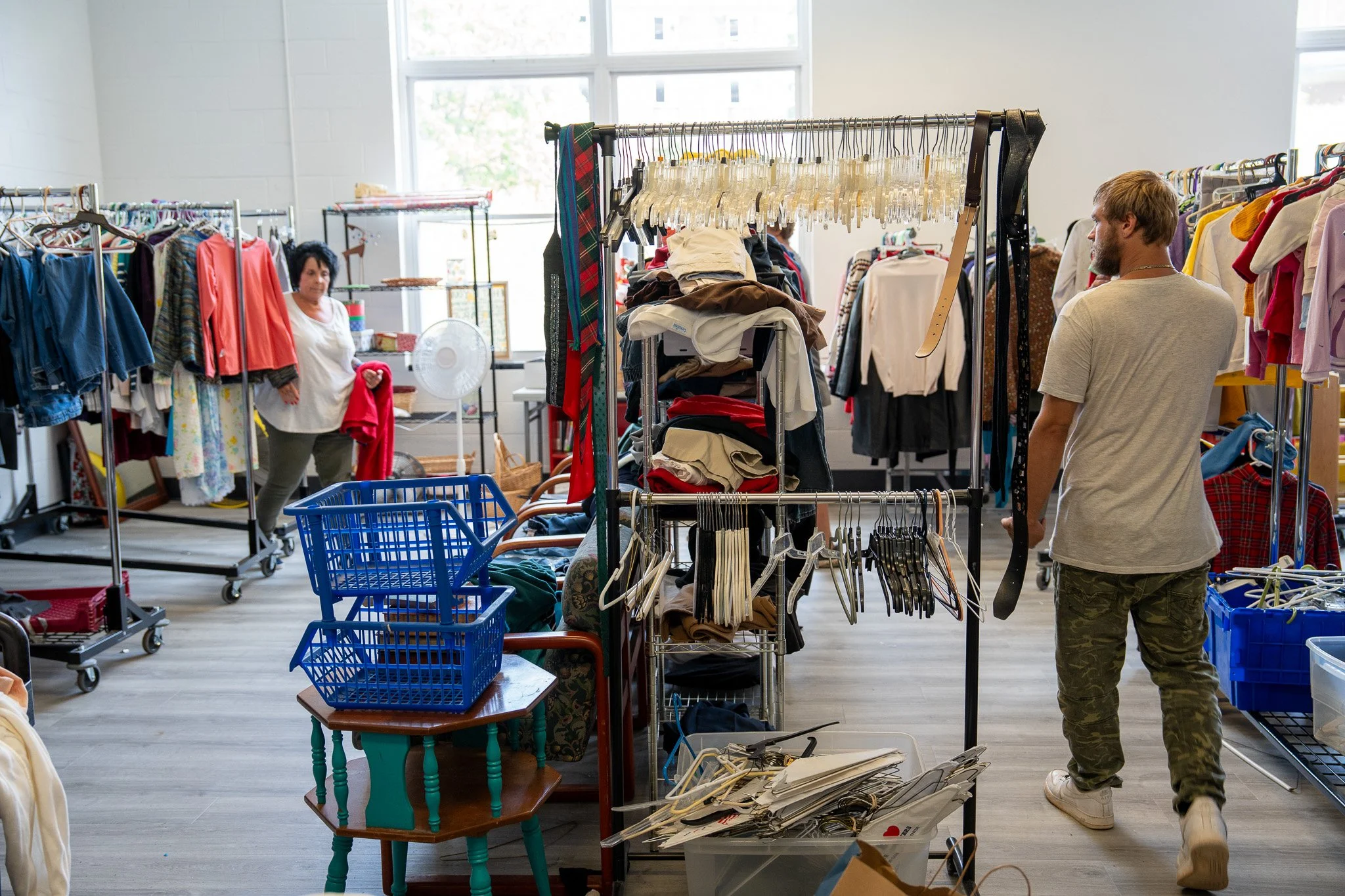 People shopping inside a thrift store with clothes racks, tables, and shopping baskets.