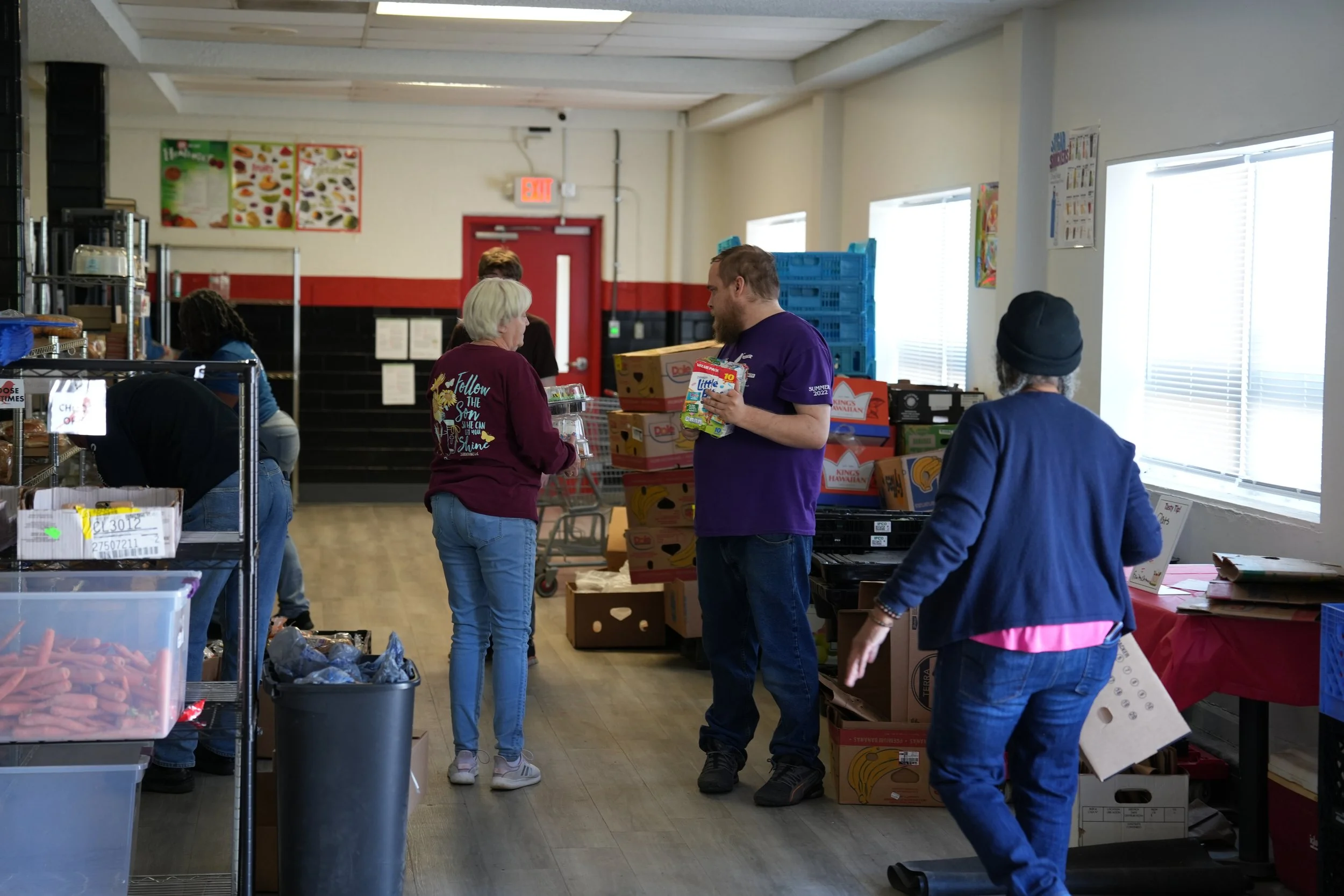 People shopping for food in a grocery store, with shelves of produce and boxed items around them.