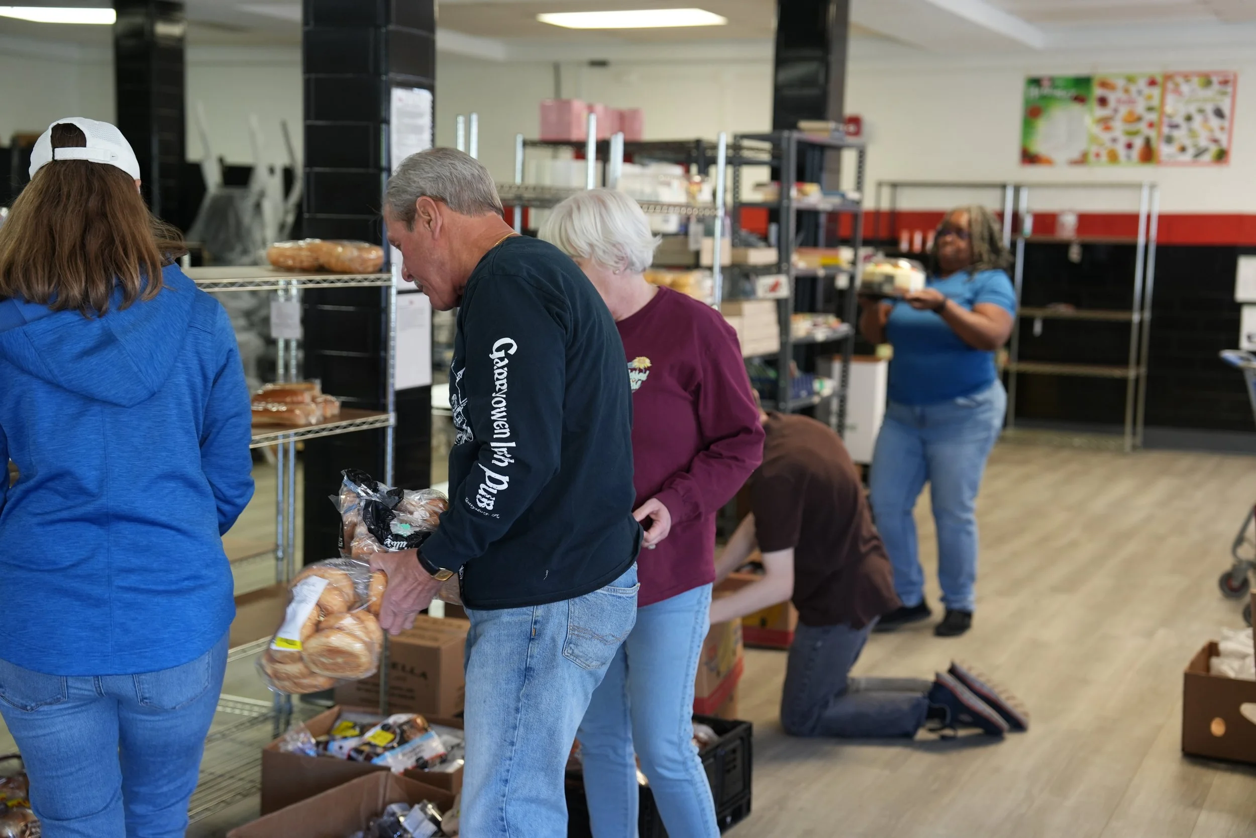 People volunteering at a food bank, sorting and packing food items on shelves and boxes.