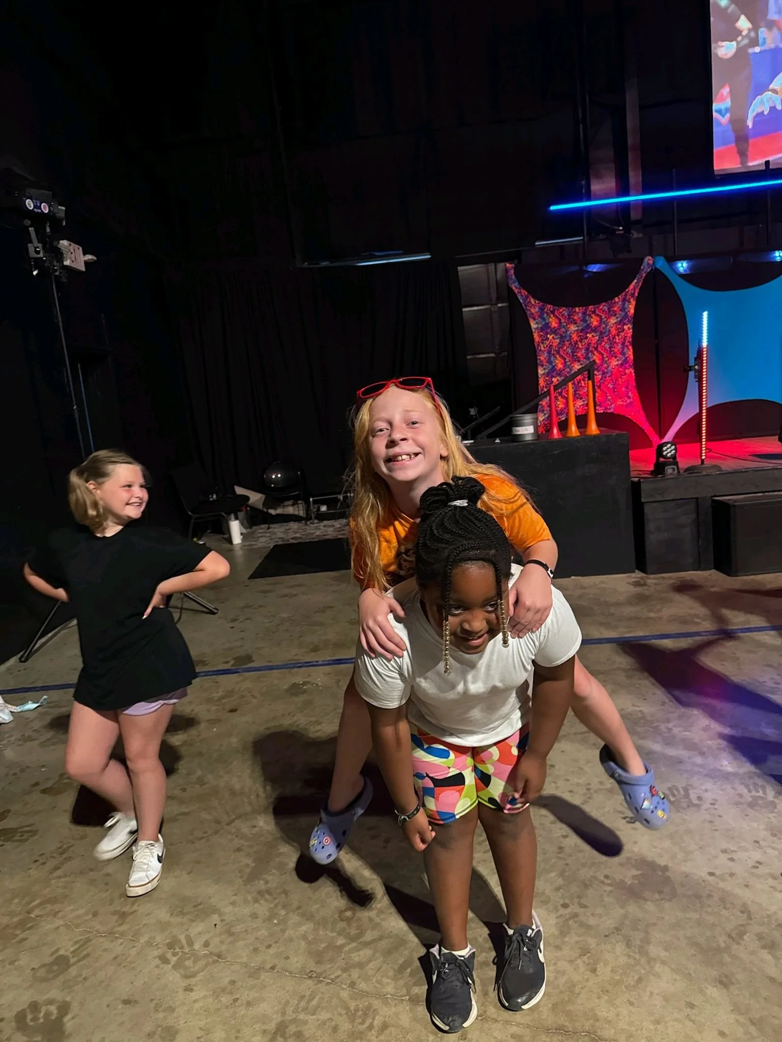 Three girls happily playing and having fun in an indoor entertainment space with a stage in the background.
