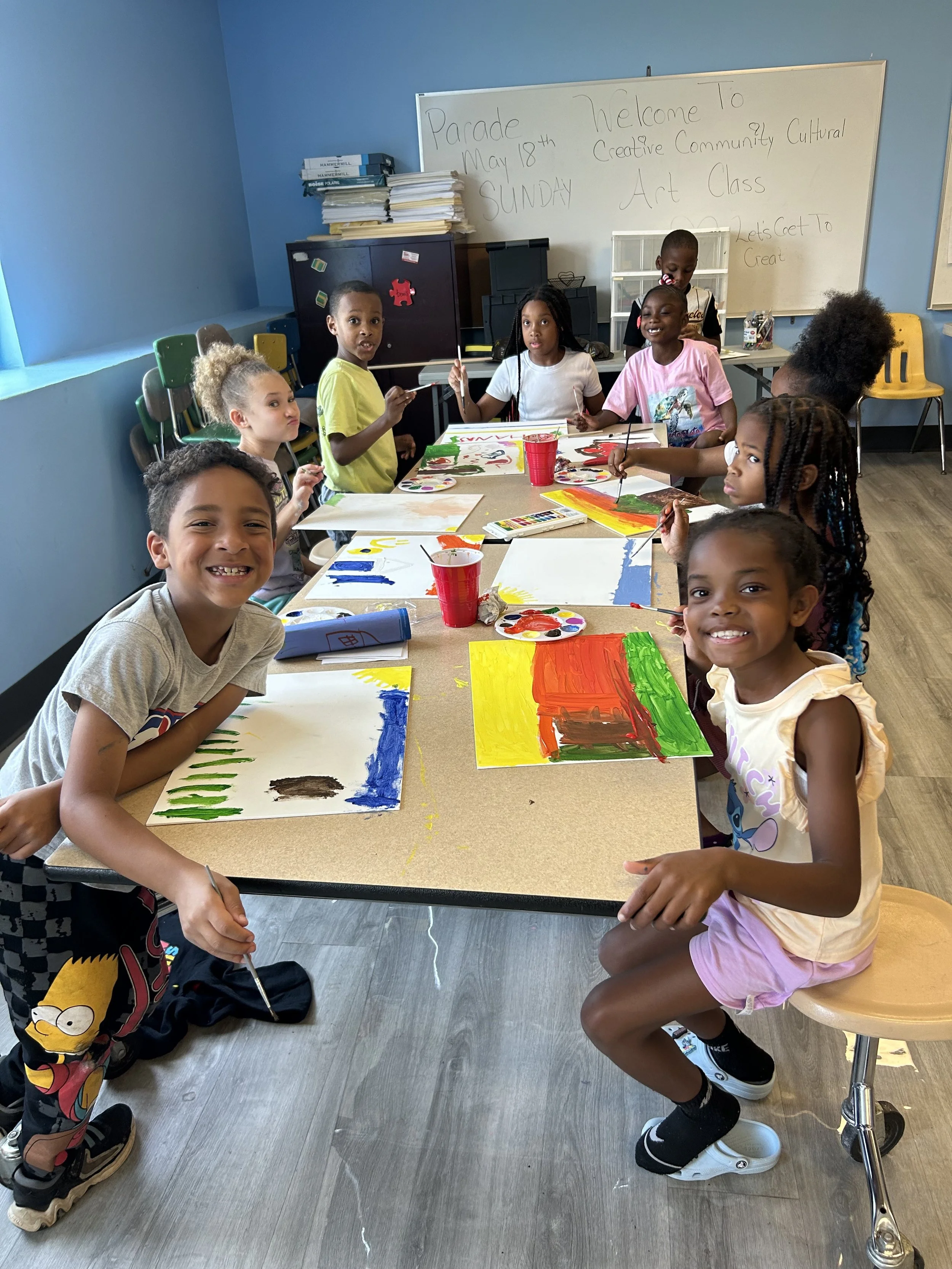Children sitting around a table painting colorful pictures in an art classroom.