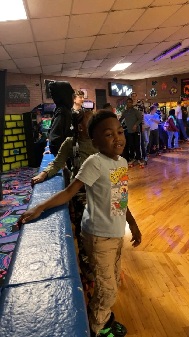Children roller skating in an indoor skating rink with colorful lighting and graffiti-style wall art.