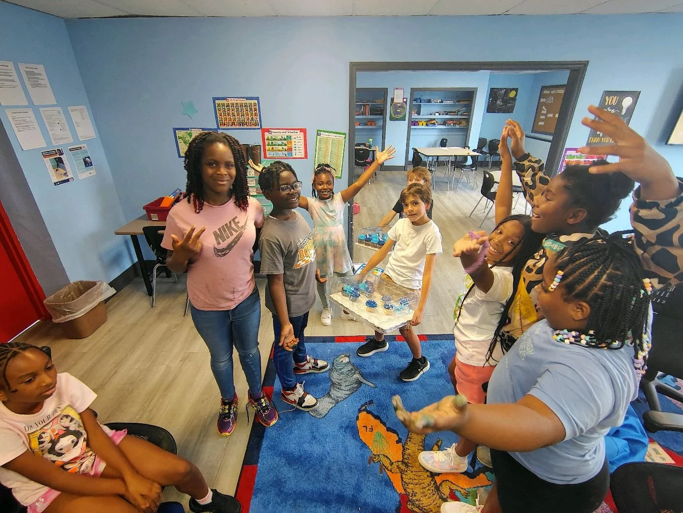 Group of children and adults in a classroom with educational posters, engaging in a hands-on activity with a crocodile model on a table