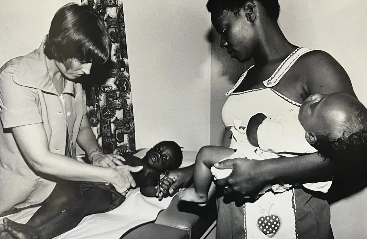 A woman is holding a crying baby, a visitor and a young child are in a hospital room.