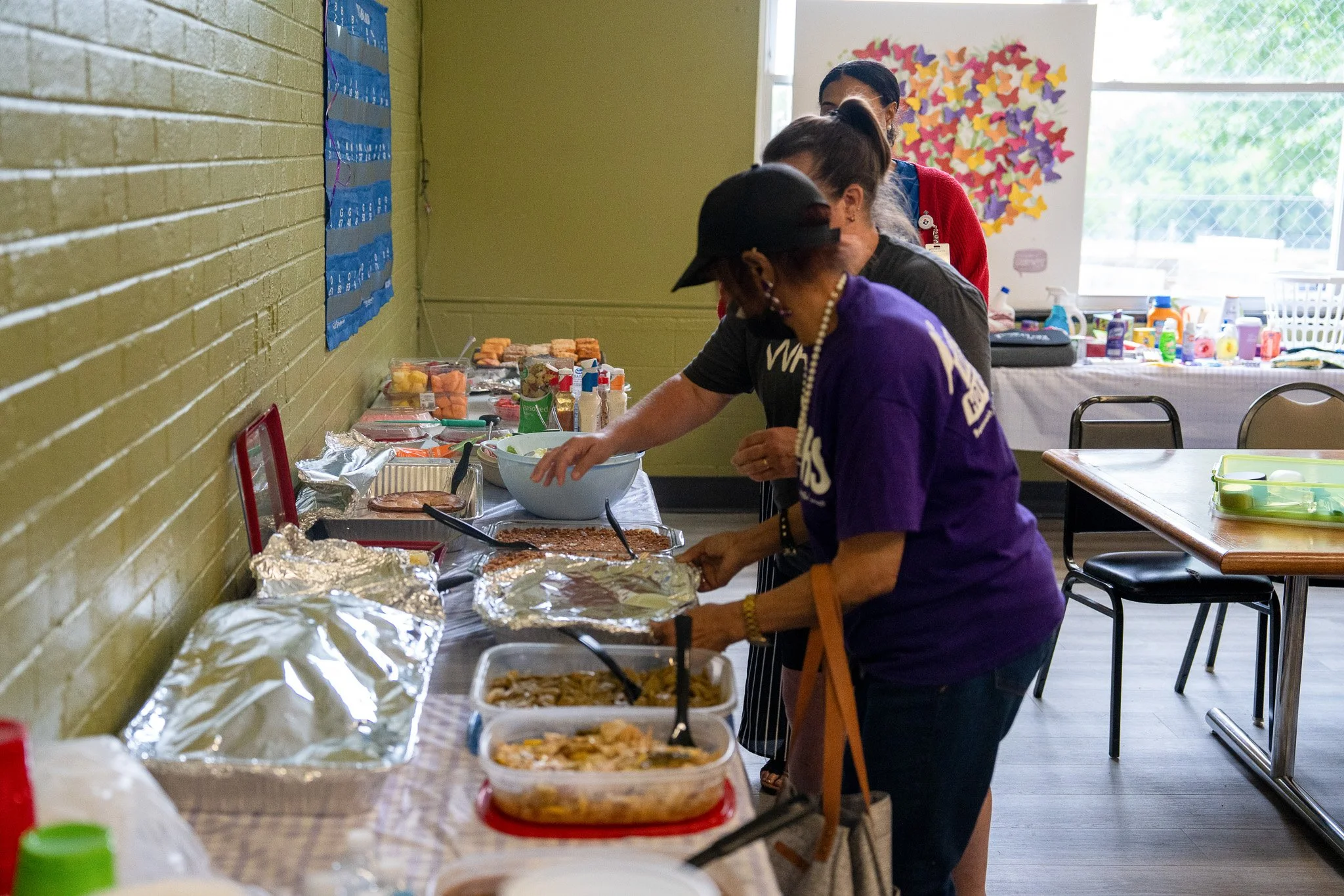 People serving themselves food from a buffet table with various dishes and desserts in a community room.