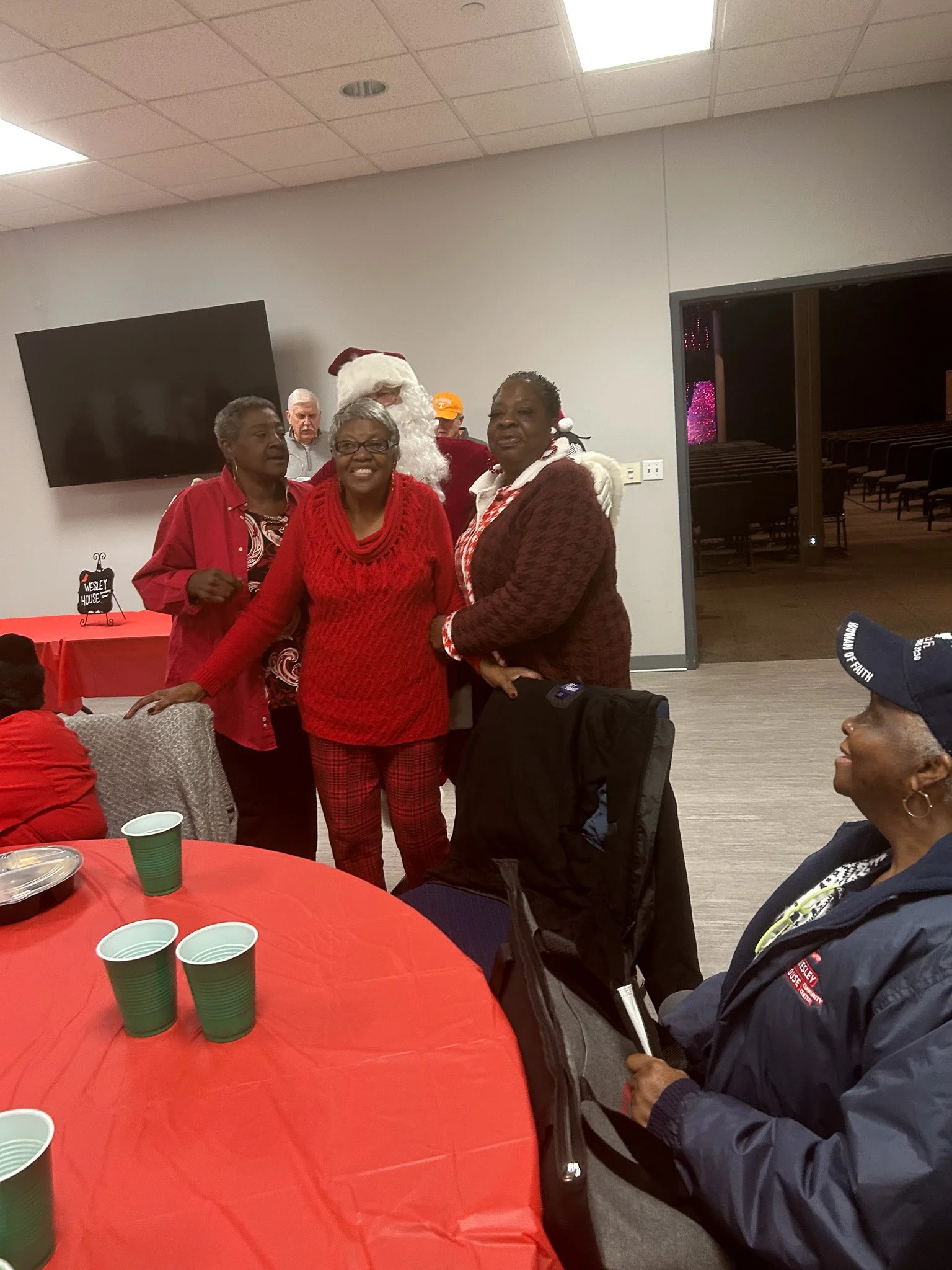 Group of people celebrating Christmas indoors, with one person dressed as Santa Claus, in a room decorated for the holiday.