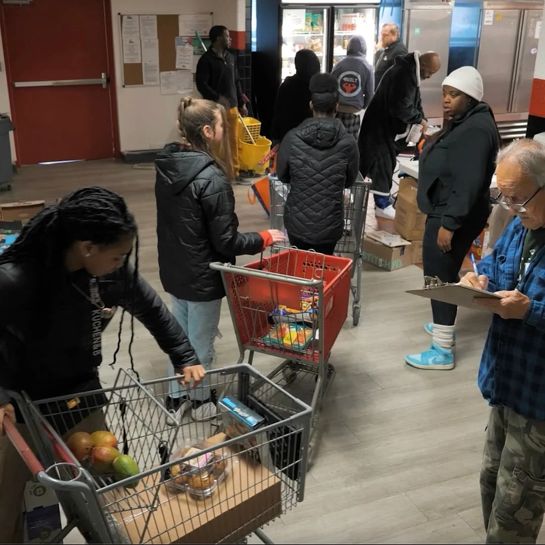 People shopping at a supermarket checkout line with shopping carts filled with groceries.