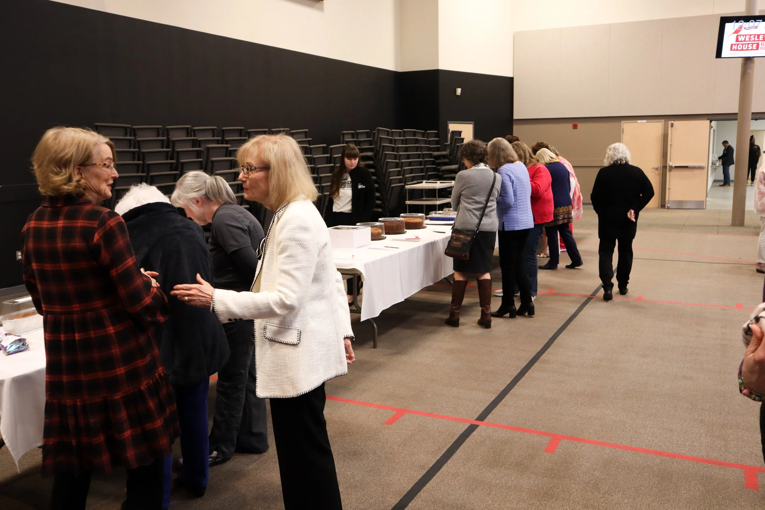 People in line at a registration or check-in table in a large indoor hall, likely at a conference or event.