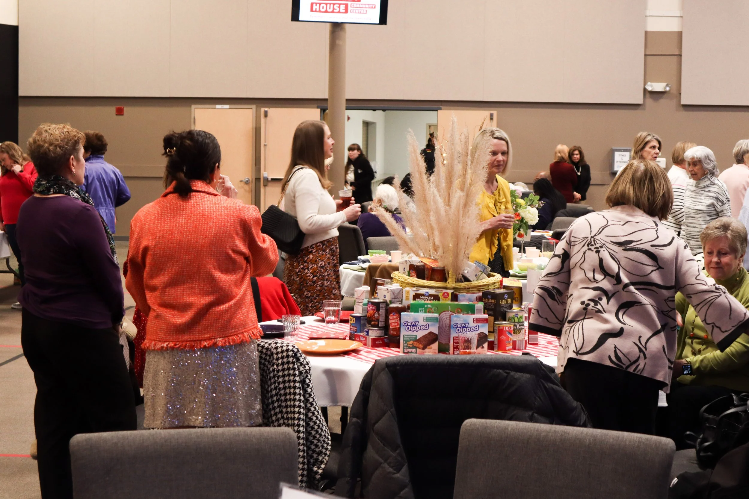People gathered around a table with food, decorations, and gift boxes at an indoor event.