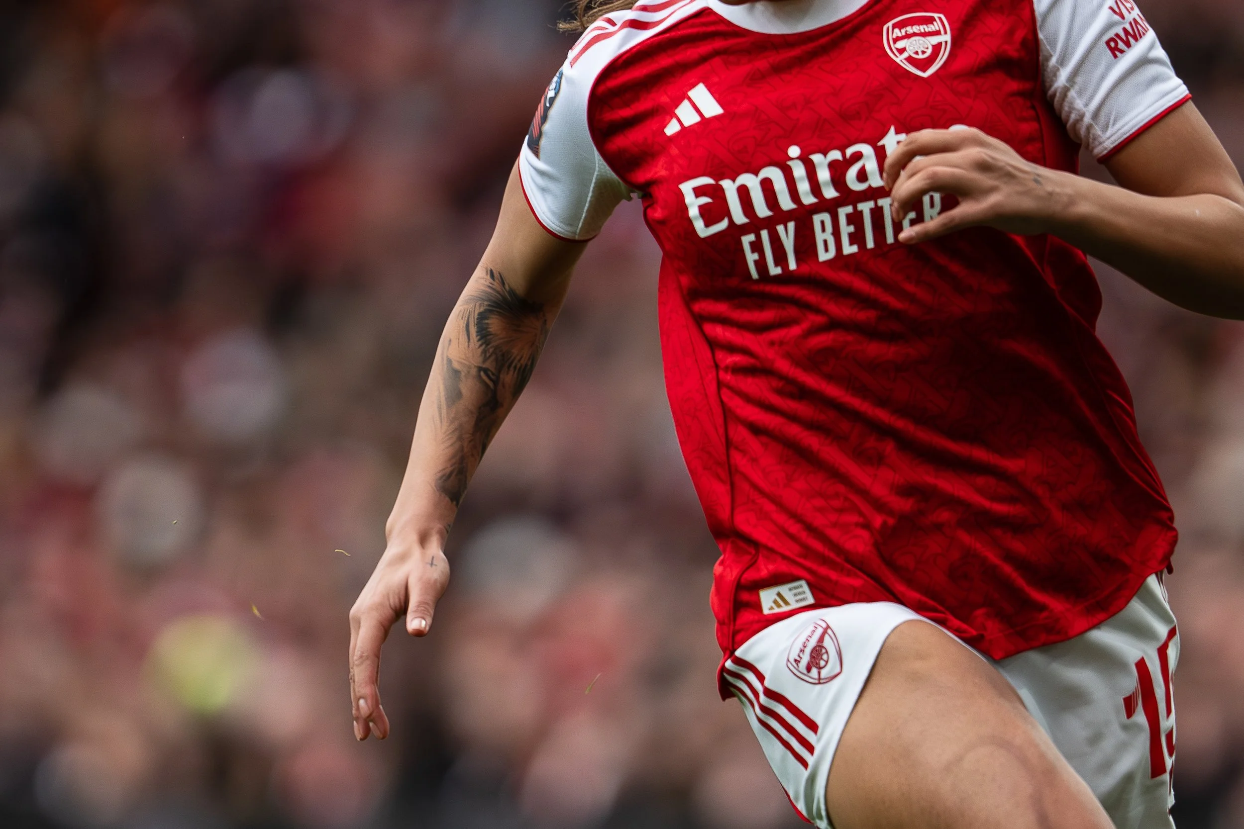 Close-up of a soccer player wearing an Arsenal jersey with visible arm tattoos during a match.