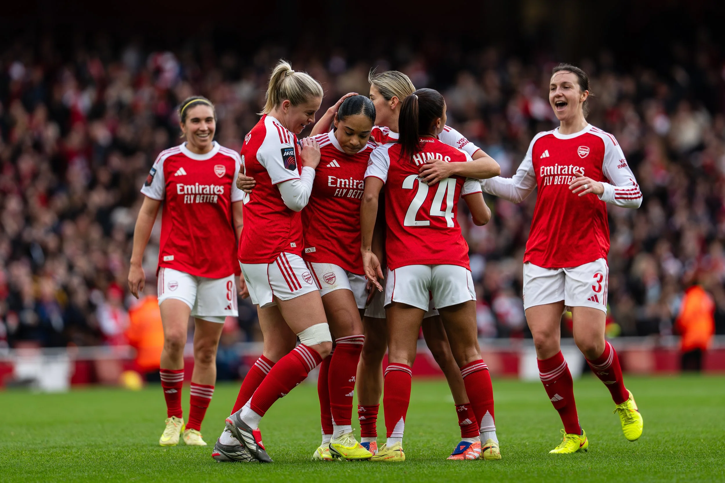 Group of women soccer players wearing red and white team jerseys celebrating on the field.