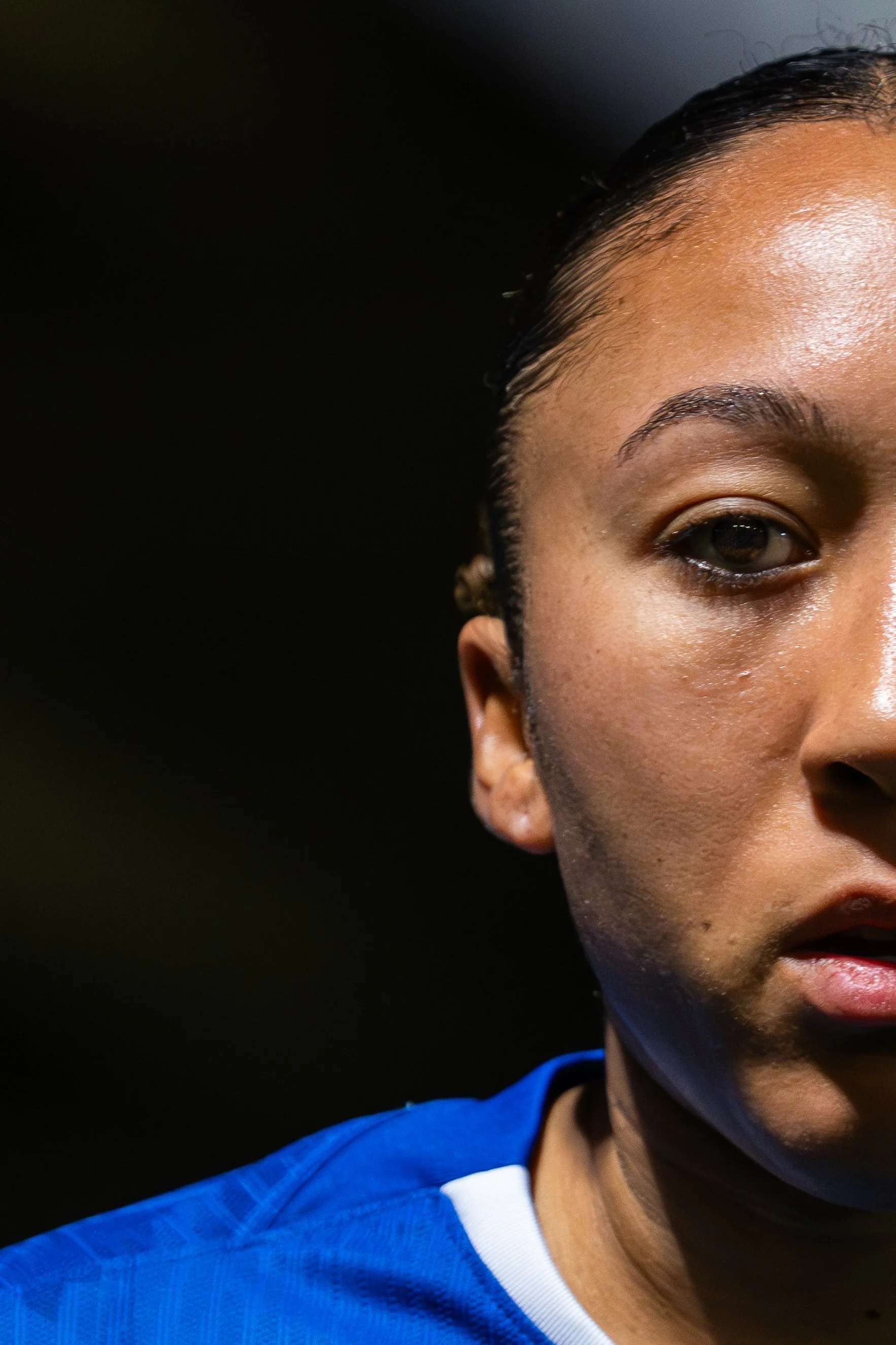 Close-up of a young man's face, showing his eye, eyebrow, forehead, and part of his cheek, with a black background.
