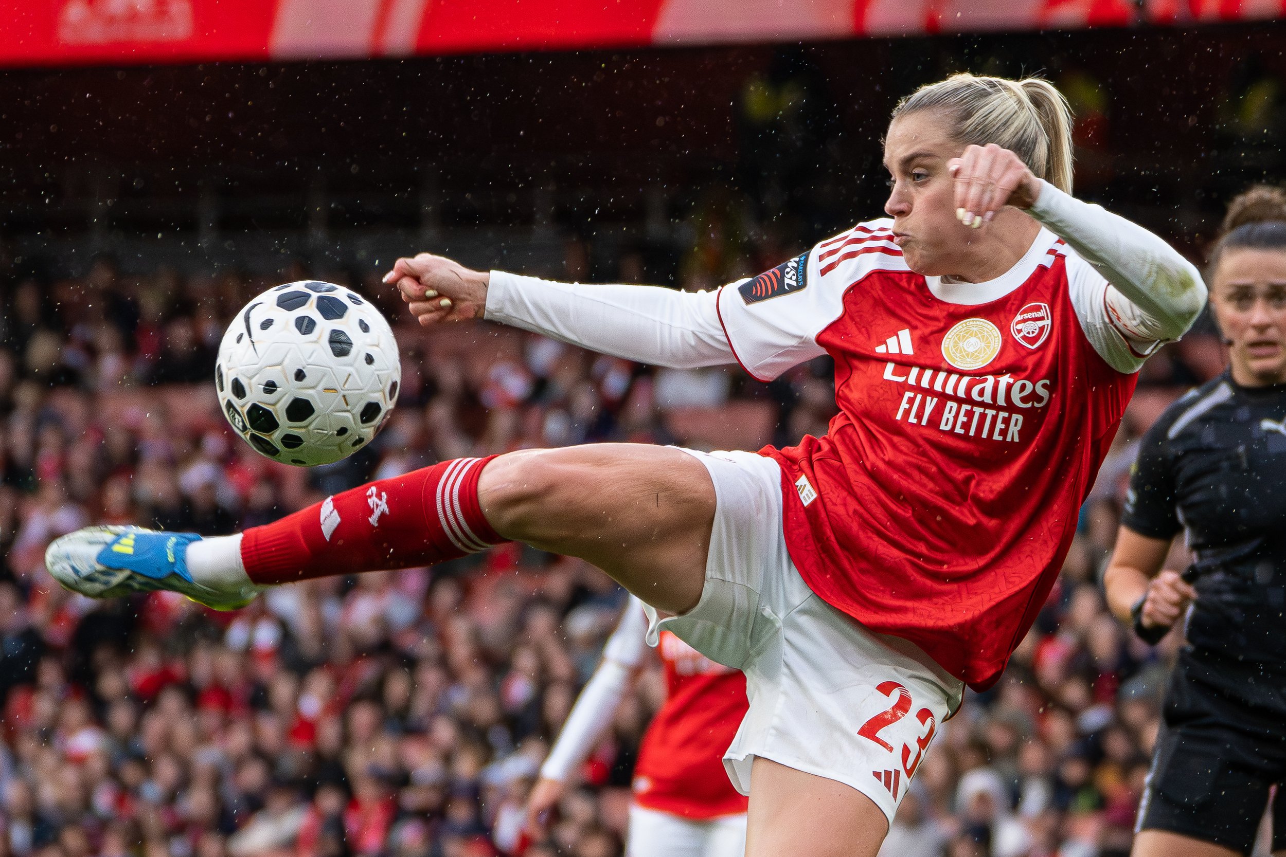 A female soccer player in a red and white jersey kicking a soccer ball during a match.