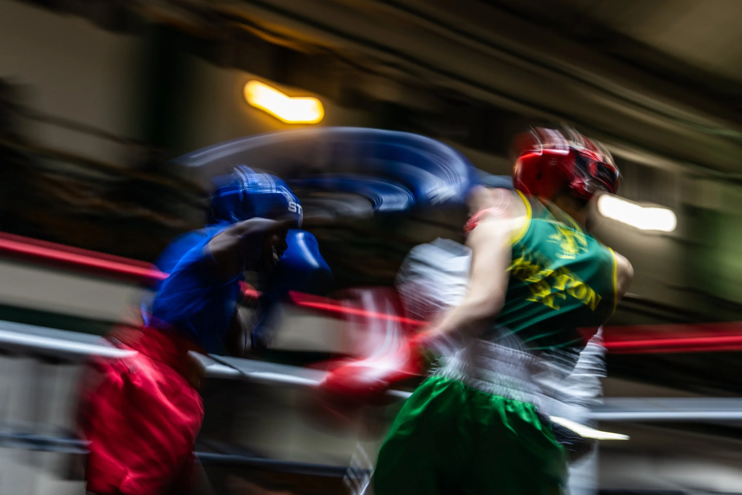 Blurred motion image of two motorcyclists racing in an underground parking garage, one wearing a blue helmet and jacket and the other wearing a red helmet and green racing outfit.