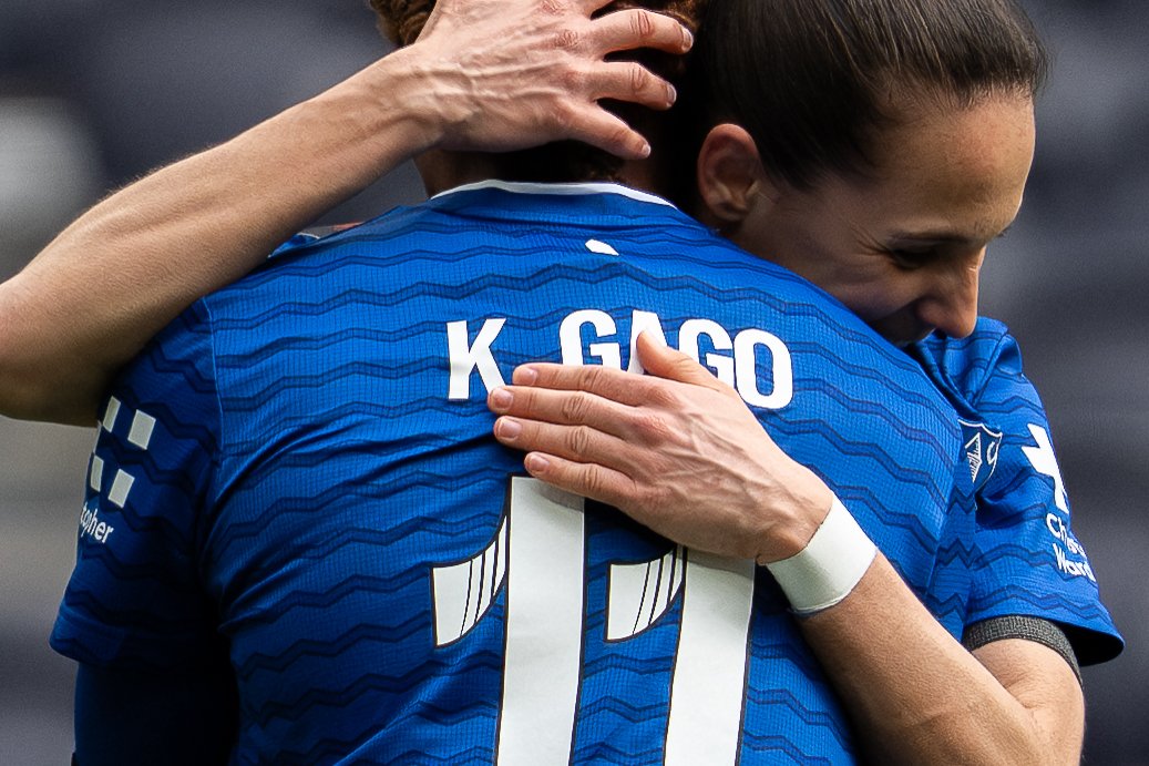 Two soccer players in blue jerseys hugging on the field.