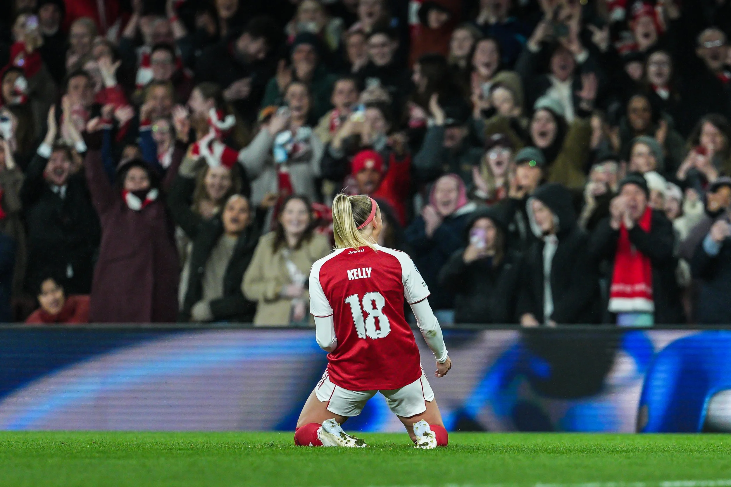 Soccer player kneeling on the field with a crowd of cheering spectators in the background.