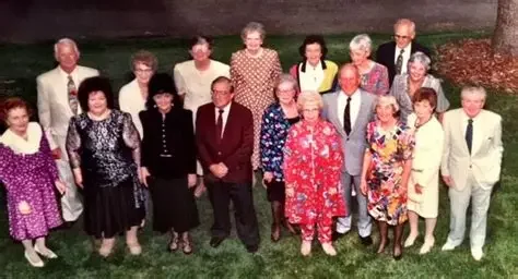 Group of fifteen people, mostly women, standing outdoors on grass with trees in the background, posing for a photo.