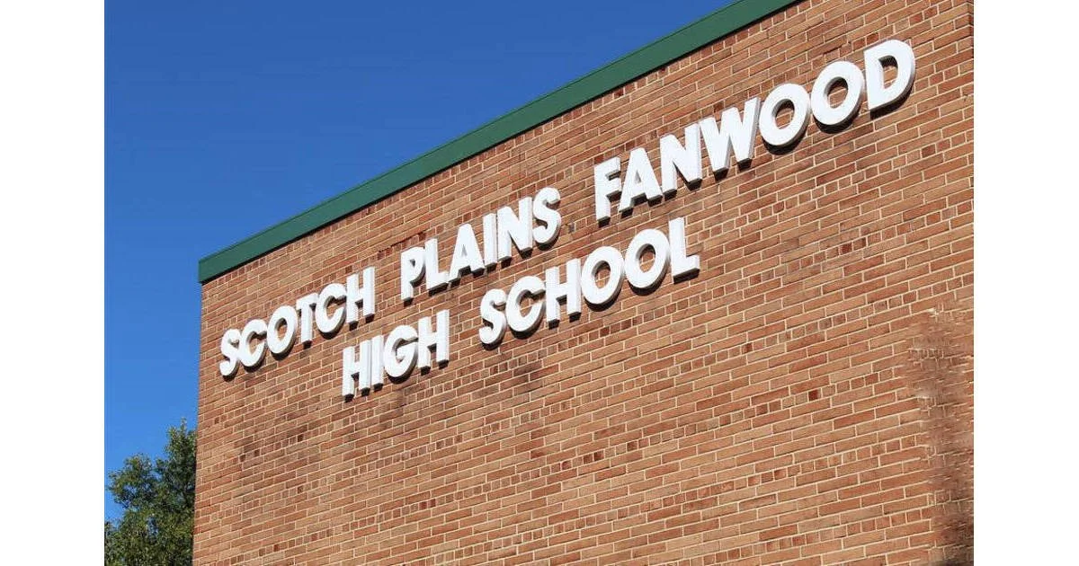 A brick school building with white 3D letters spelling 'Scotch Plains Fanwood High School' on the exterior wall, against a clear blue sky.