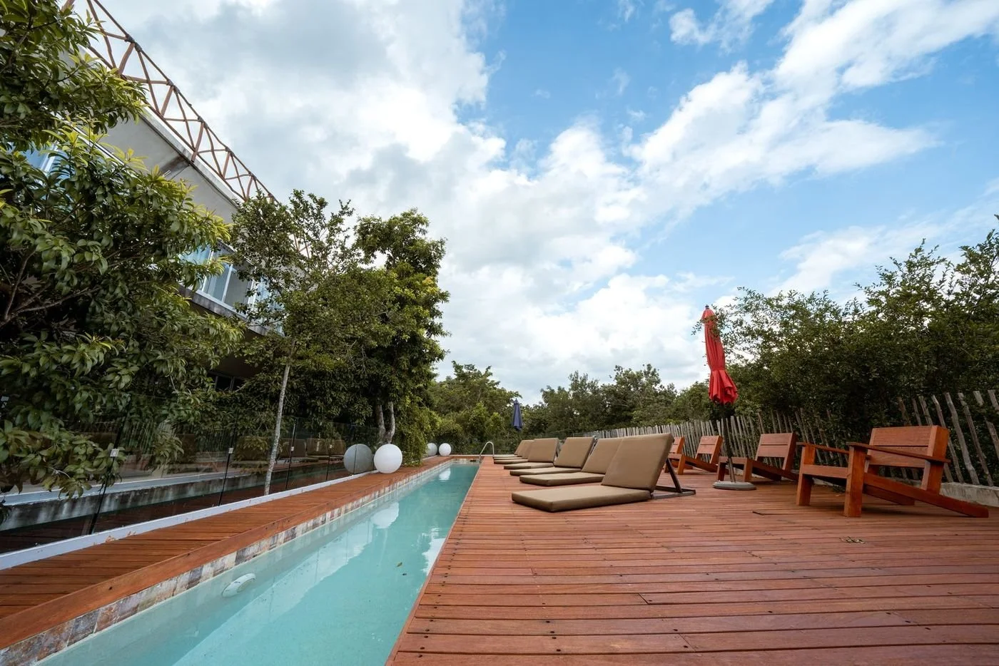 long bright blue pool on wooded deck with sun loungers and umbrella surrounded by trees